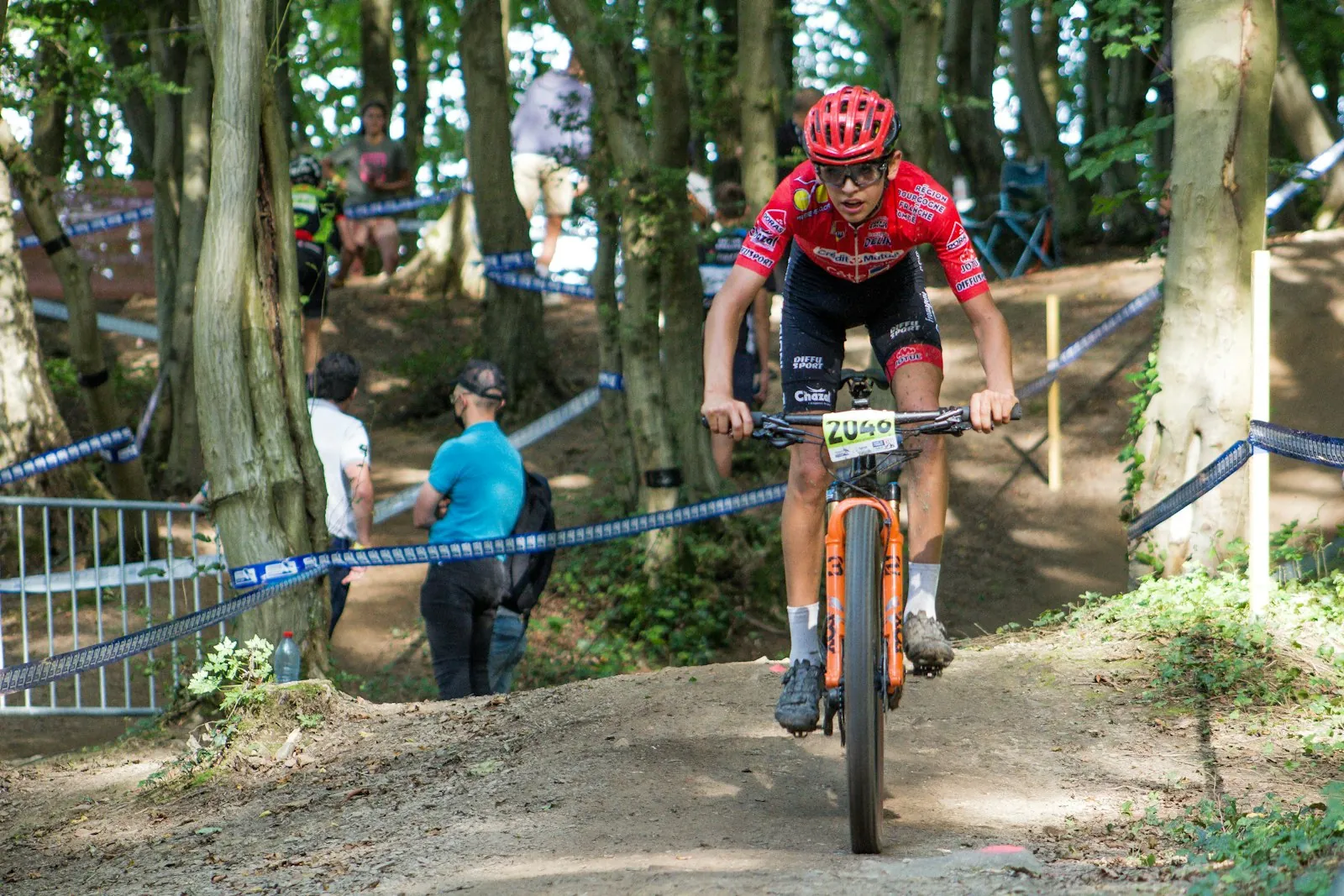 Corredor de XCO con dorsal bajando entre cintas de carrera en el bosque